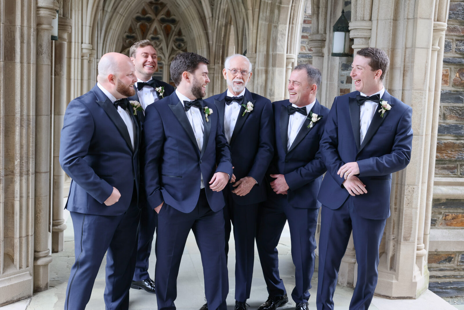 Grooms in blue tux with groomsmen in matching blue tuxes at duke chapel laughing and having fun