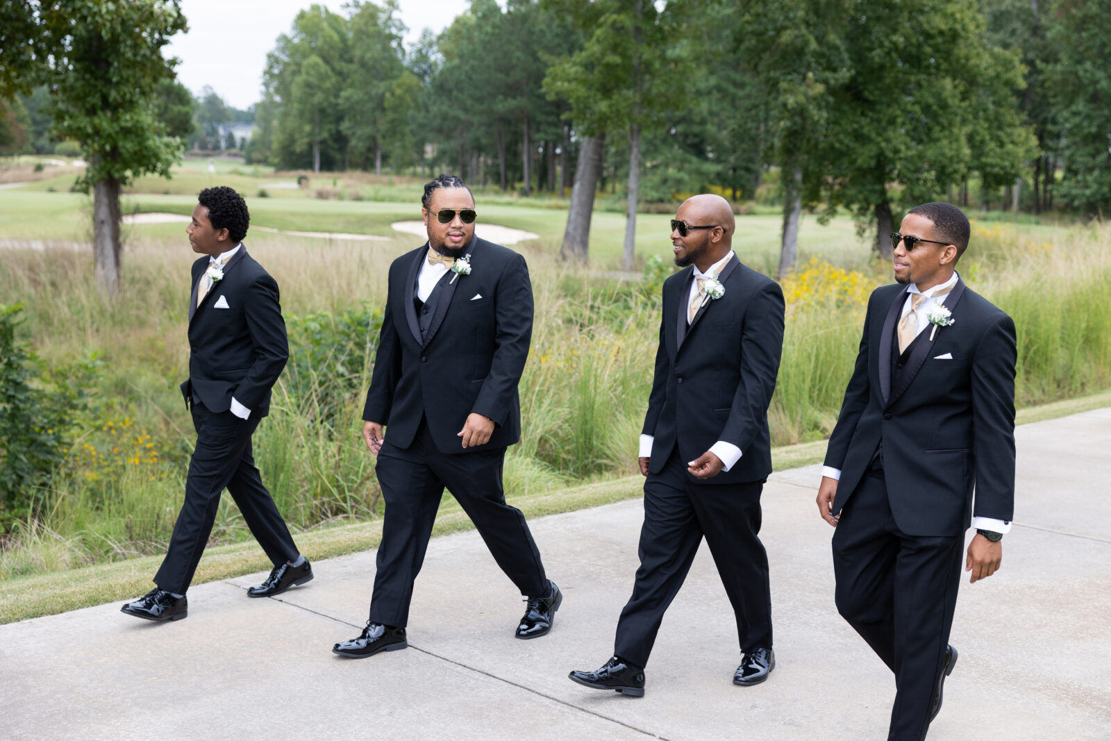 Groom in black tux walking at Twin Oaks Country Club walking with groomsmen also in black tuxes 