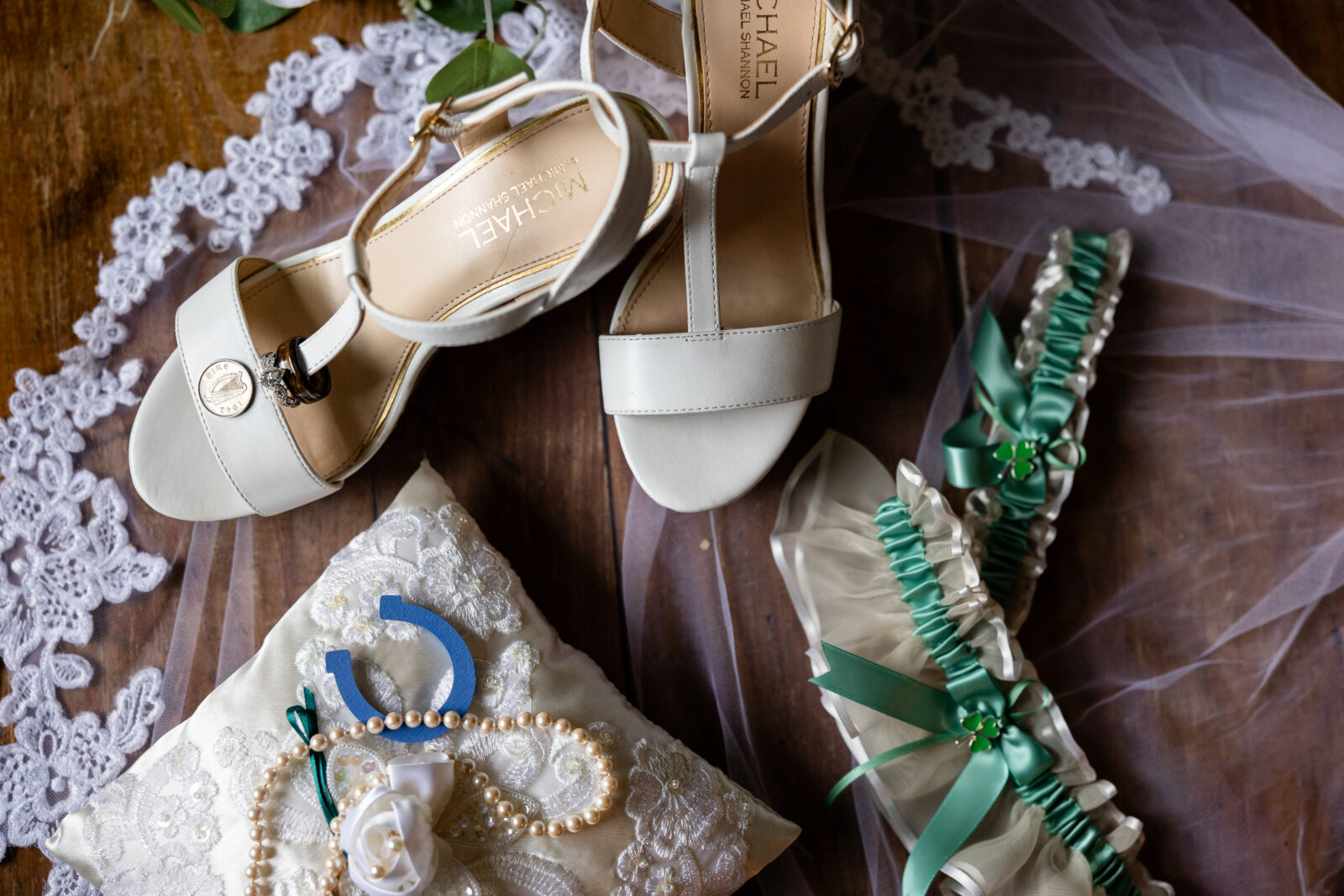 Top down photo of brides shoes with half pence, st patty's day themed wedding, green garter belt, ringbearer pillow, lace detailed veil, and vintage engagement ring