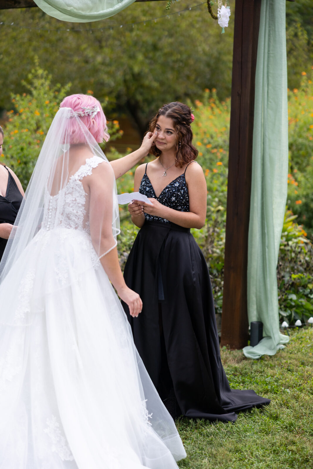 Bride in big white taffeta dress wiping tears of her bride in a black dress with beaded detailing reading vows at Tranquility estate 
