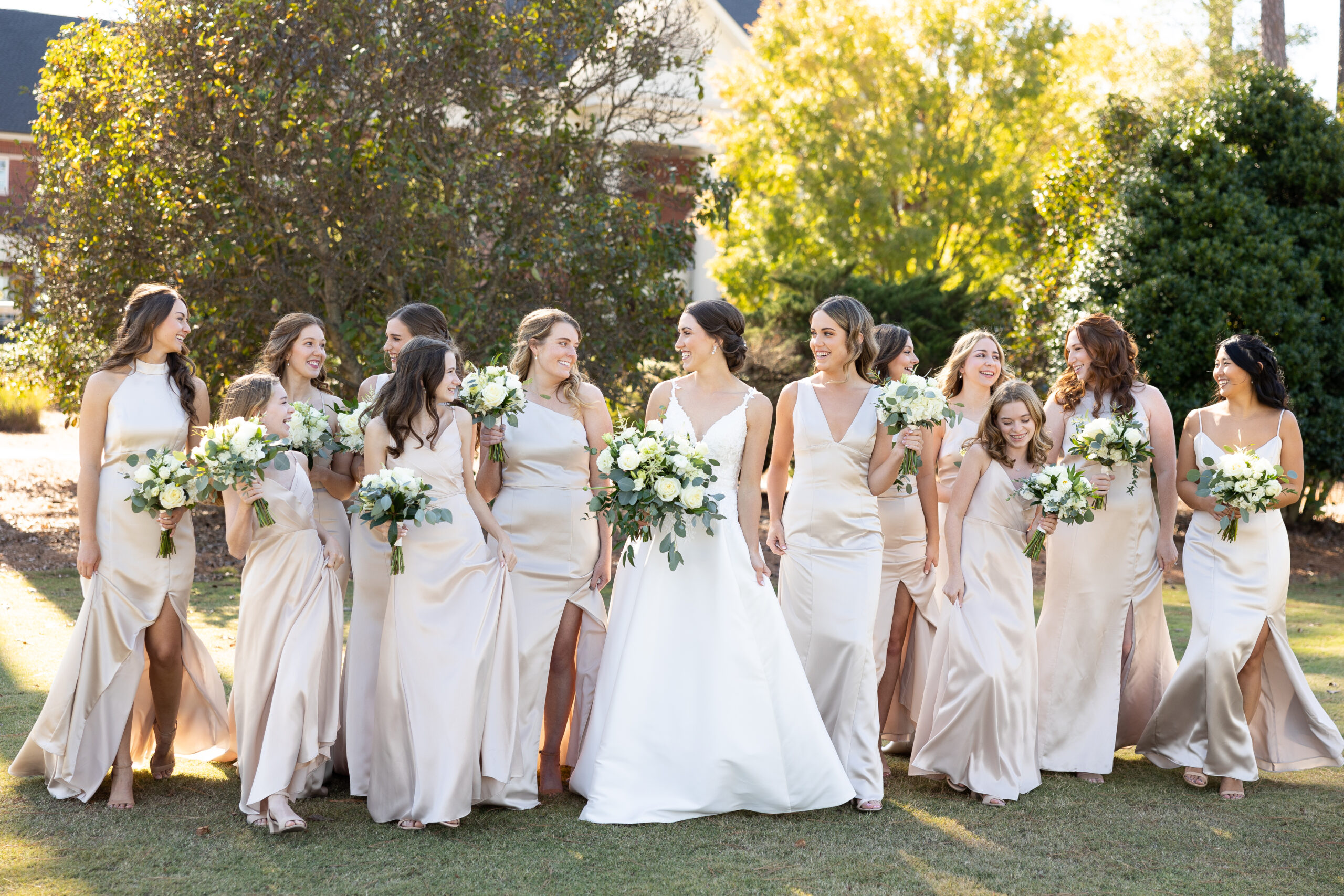 Bride in elegant white plunging v neck wedding dress walking with bridesmaids in champagne bridesmaid dresses over golf course in Durham NC
